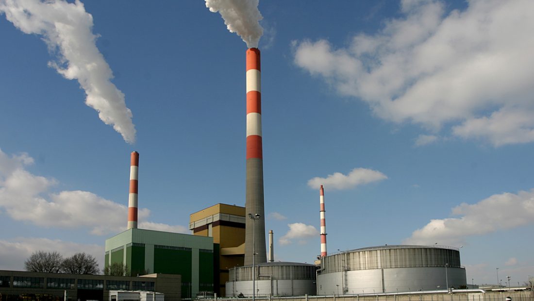 Außenaufnahme des Kraftwerks Simmering, mit hohen Schornsteinen, die weißen Rauch vor einem blauen Himmel mit vereinzelten Wolken ausstoßen.