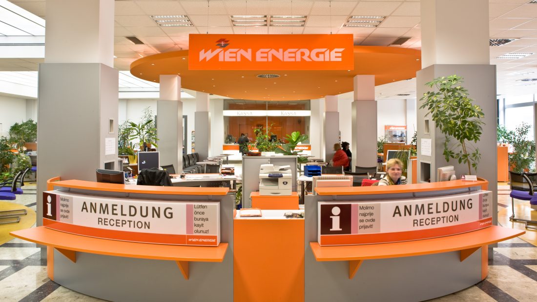 Orangefarbener Empfangsbereich von Wien Energie mit Schreibtischen, Stühlen und Topfpflanzen.
