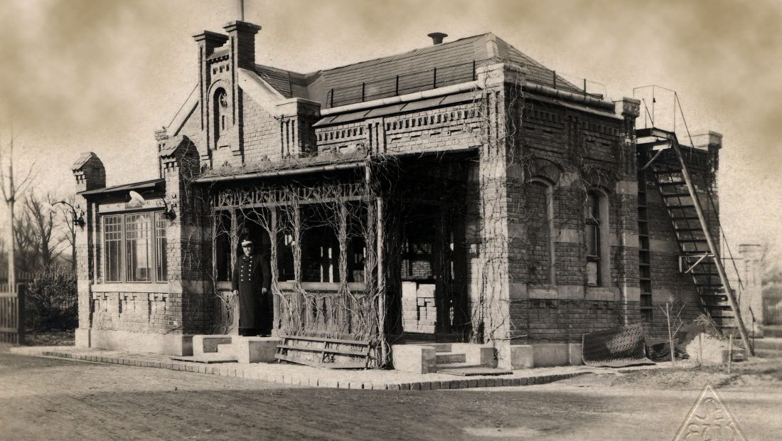 Historisches Foto eines Backsteingebäudes, welches die Portierloge im Kraftwerk SImmering war, mit reich verzierter Veranda und Außentreppe inmitten einer kargen Landschaft.