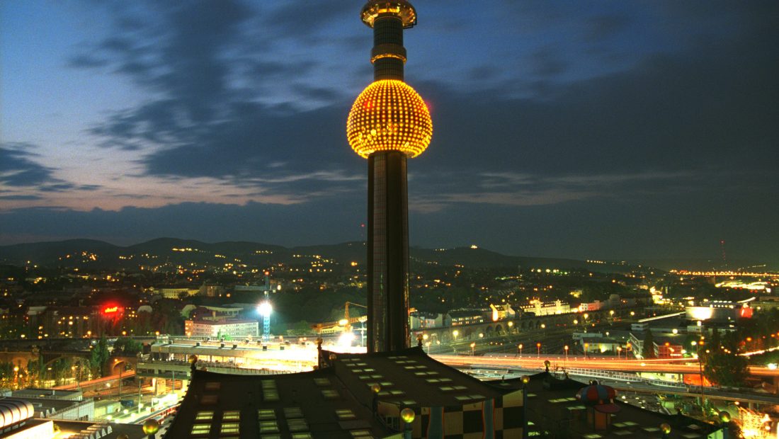 Nachtansicht der Abfallverwertungsanlage Spittelau mit der Wiener Skyline im Hintergrund und dunklem, bewölktem Himmel.