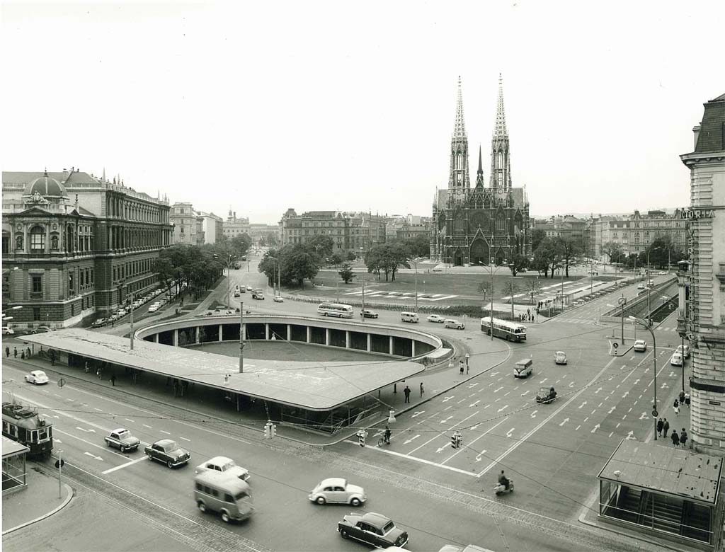 Stadtansicht mit der Votivkirche, einem Kreisverkehr, Oldtimern und historischen Gebäuden in einem Schwarzweißfoto.