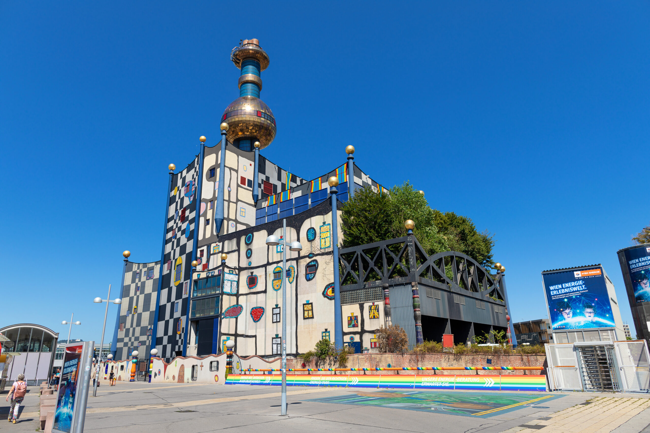 Die Abfallverwertungsanlage Spittelau - ein
farbenfrohes, vielseitiges Gebäude mit goldener Kuppel und künstlerischer Fassade unter strahlend blauem Himmel.