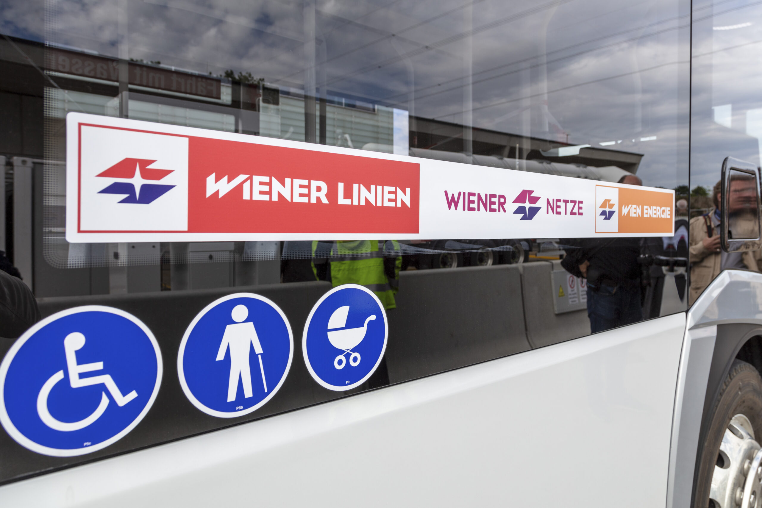 Seite eines Busses mit dem Logo der Wiener Linien, Wiener Netze und Wien Energie mit Symbolen für Barrierefreiheit, einschließlich Rollstuhl, Gehhilfe und Kinderwagen.