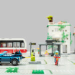 Lego-City-Szene mit einem Radfahrer, einem aufladenden Elektroauto, einer Straßenbahn im Hintergrund und einer Ampel.