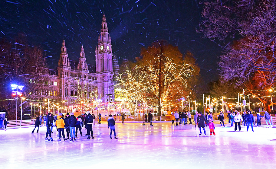 Auf der wunderschön beleuchteten Eisbahn des Wiener Eistraums vor dem Wiener Rathaus  laufen Menschen Schlittschuh.