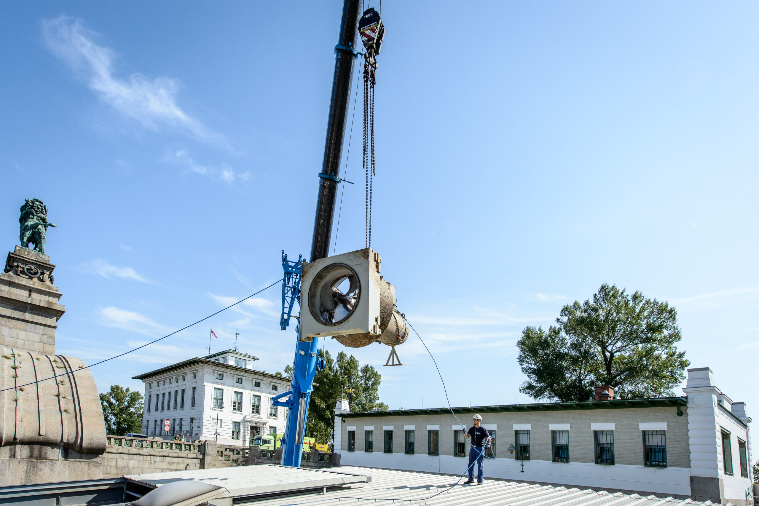 Ein Kran hebt die Hydro-Matrixturbinen in das Kraftwerk Nussdorf. Im Hintergrund ist Wien bei klaren Himmel zu sehen.