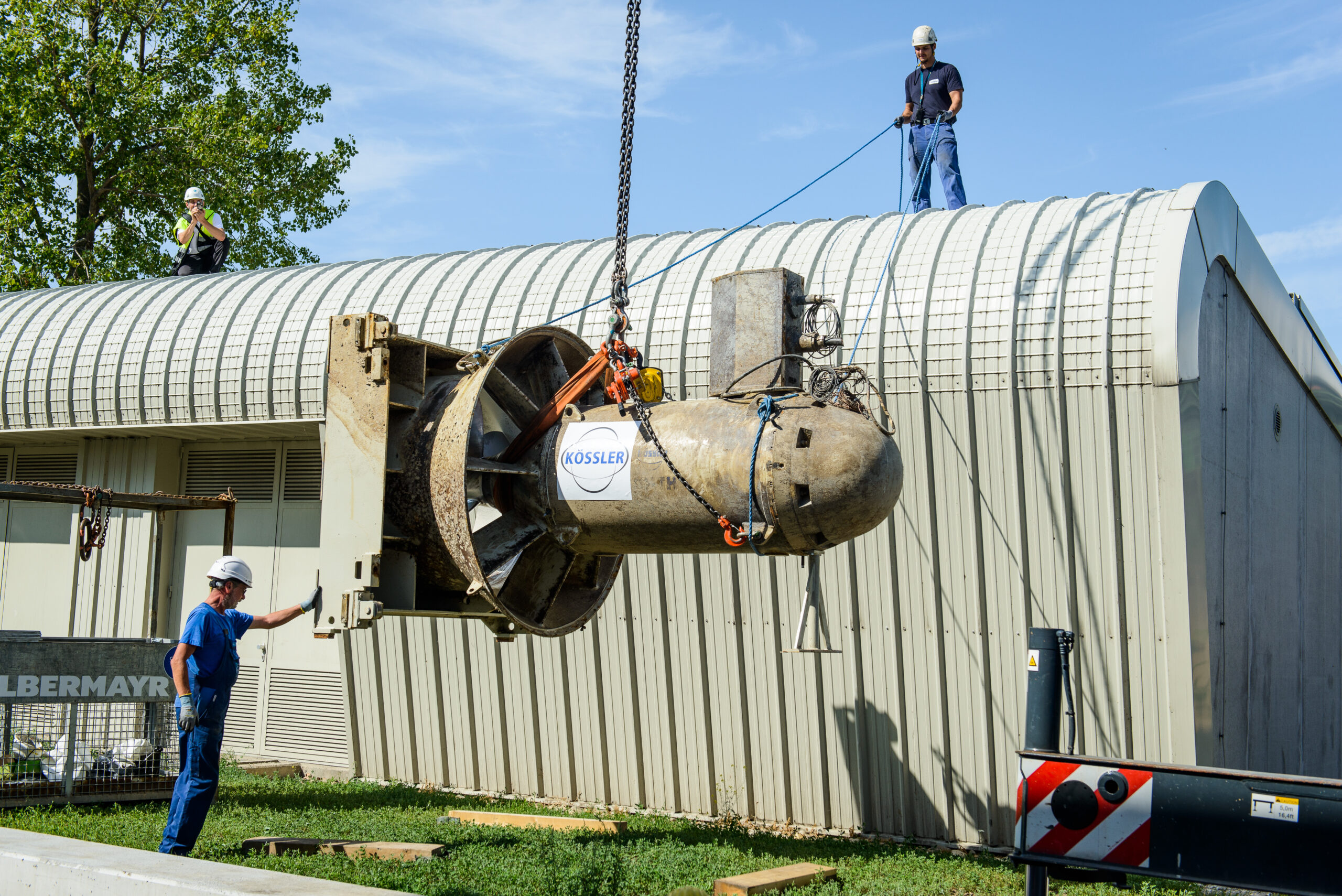 Ein Kran hebt die Hydro-Matrixturbinen in das Kraftwerk Nussdorf. Im Hintergrund ist Wien bei klaren Himmel zu sehen.