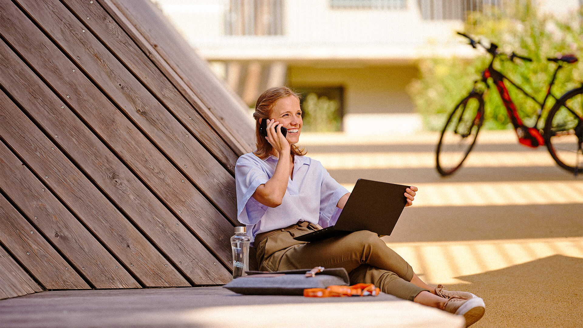 Frau sitzt in der Sonne und arbeitet am Laptop.