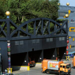 Orangefarbene Müllwagen parken vor der einzigartig gestalteten Abfallbehandlungsanlage Spittelau, mit Bäumen auf dem Dach und farbenfrohen Dekorationen.