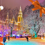 Schlittschuhläufer erfreuen sich nachts beim Wiener Eistraum am Rathausplatz an einer beleuchteten Winterlandschaft mit reich verzierten Gebäuden und geschmückten Bäumen.