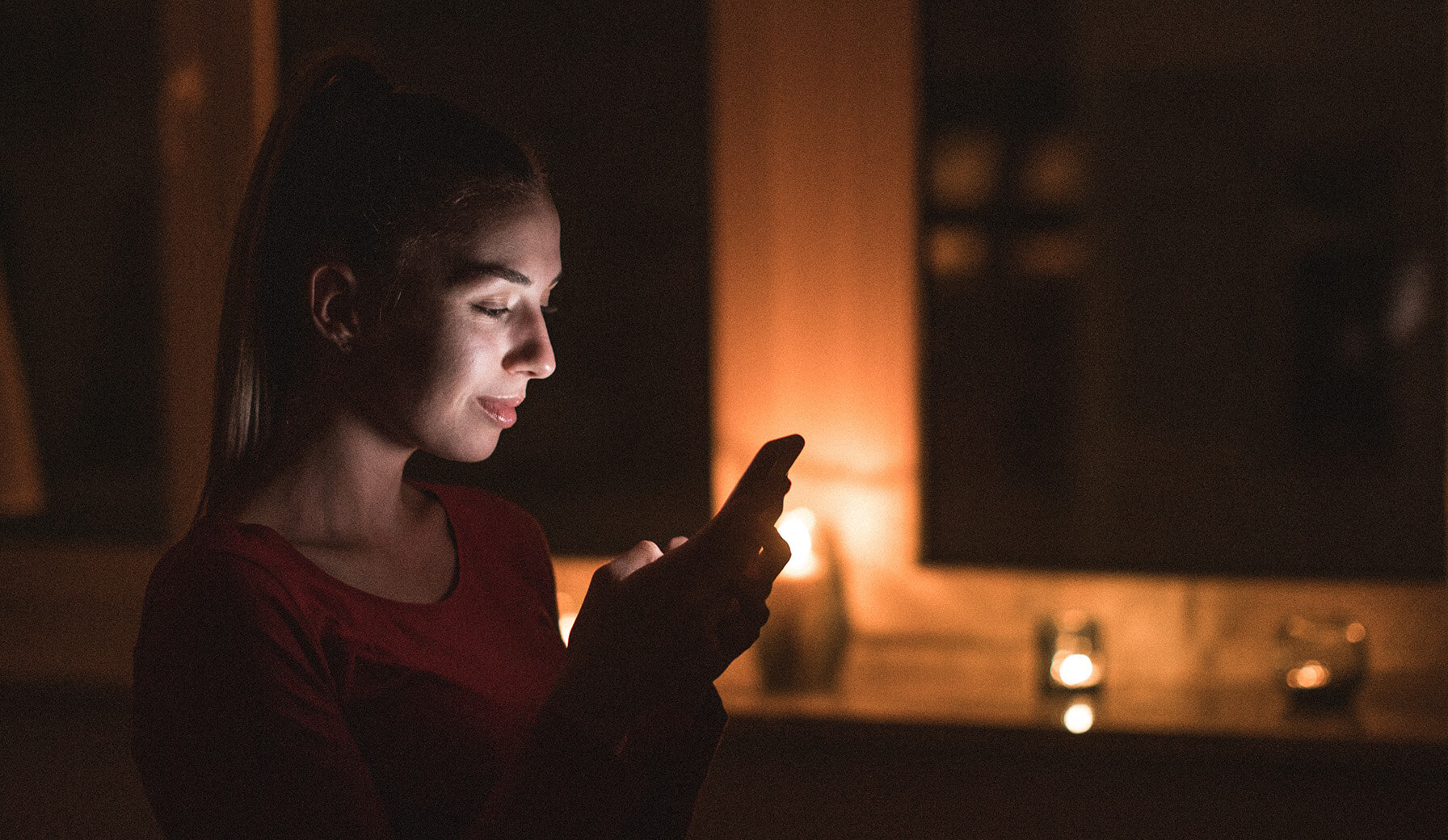 Frau steht im Dunkeln mit Kerze im Hintergrund