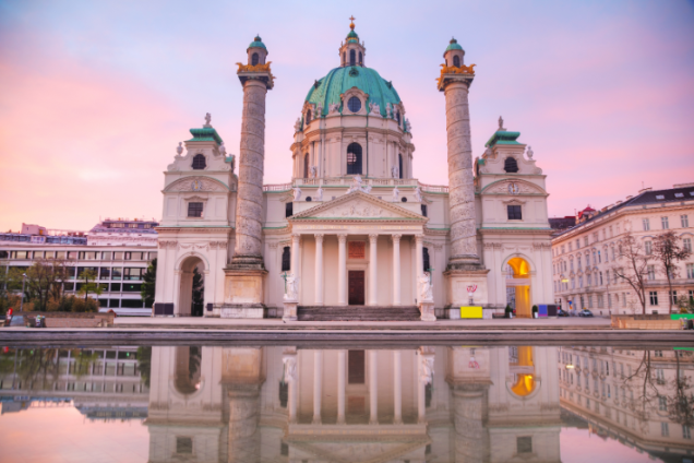 Die Karlskirche in Wien spiegelt sich wunderschön im Wasser, mit einem farbenprächtigen Sonnenuntergangshimmel im Hintergrund.