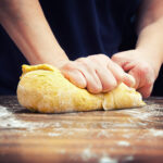 Eine Person knetet Teig auf einer bemehlten Holzoberfläche.