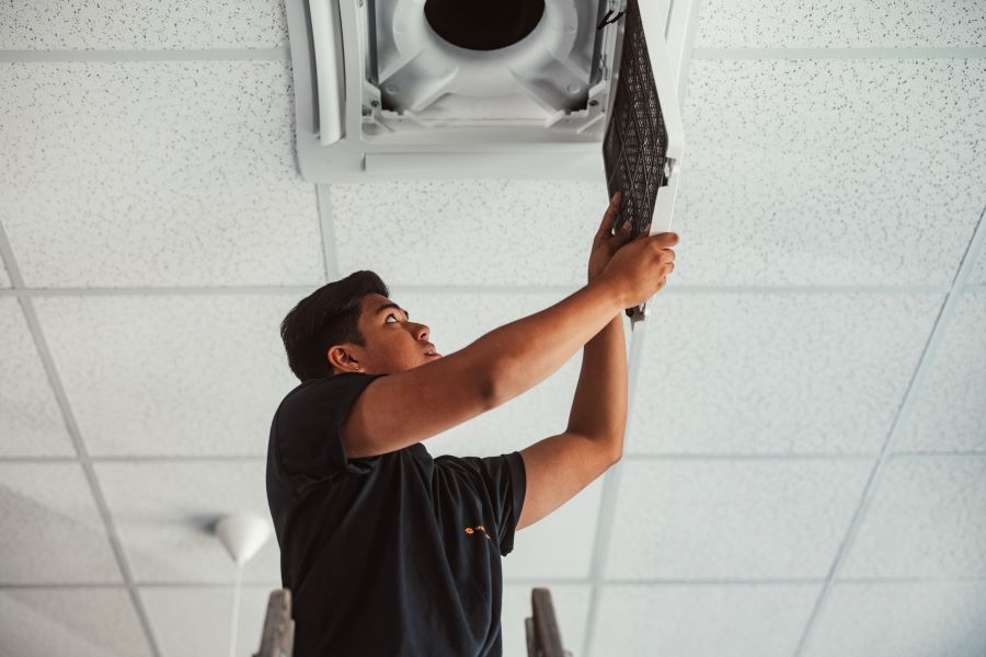 Lehrling repariert Klimaanlage an Zimmerdecke