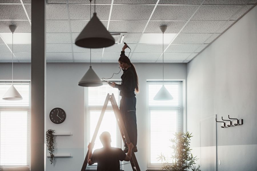 Lehrling auf Stehleiter überprüft Klimaanlage