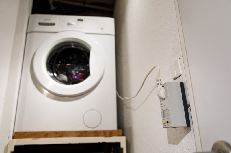 Frontlader-Waschmaschine in einer Ecke, angeschlossen an ein Strommessgerät.