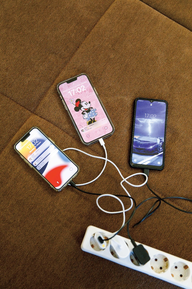 Drei Smartphones werden auf einem braunen Teppich aufgeladen und an eine Steckdosenleiste angeschlossen.