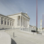 Elegantes Parlamentsgebäude von Wien mit großen Säulen, Skulpturen und an klaren Tagen wehenden Flaggen; eine Rampe führt elegant zum Eingang.
