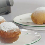 Teller mit gezuckerten Krapfen auf einer Arbeitsplatte.
