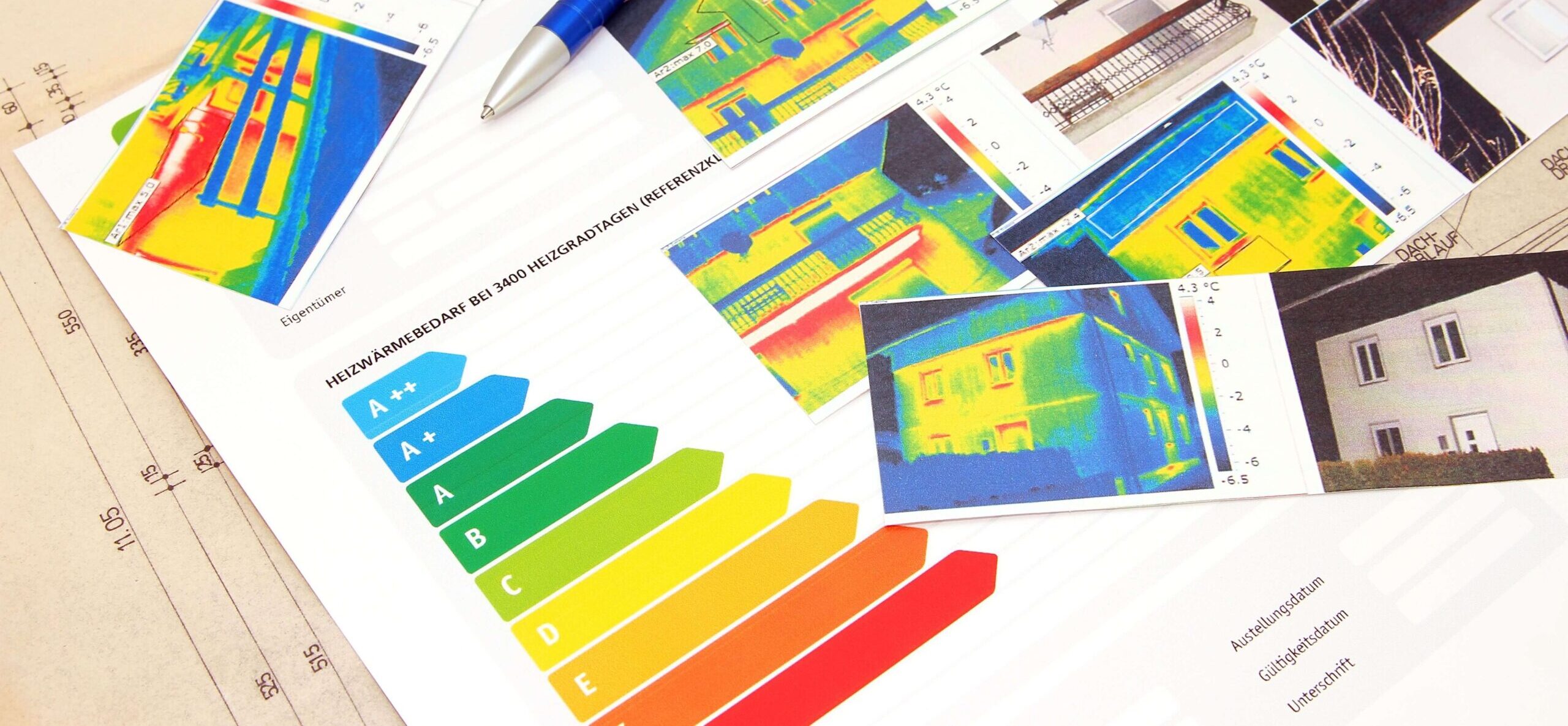 Wärmebilder, Energieausweis, Stift und Baupläne auf einem Tisch.