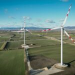 Windturbinen auf einer riesigen grünen Wiese in Trumau unter einem blauen Himmel mit vereinzelten Wolken.