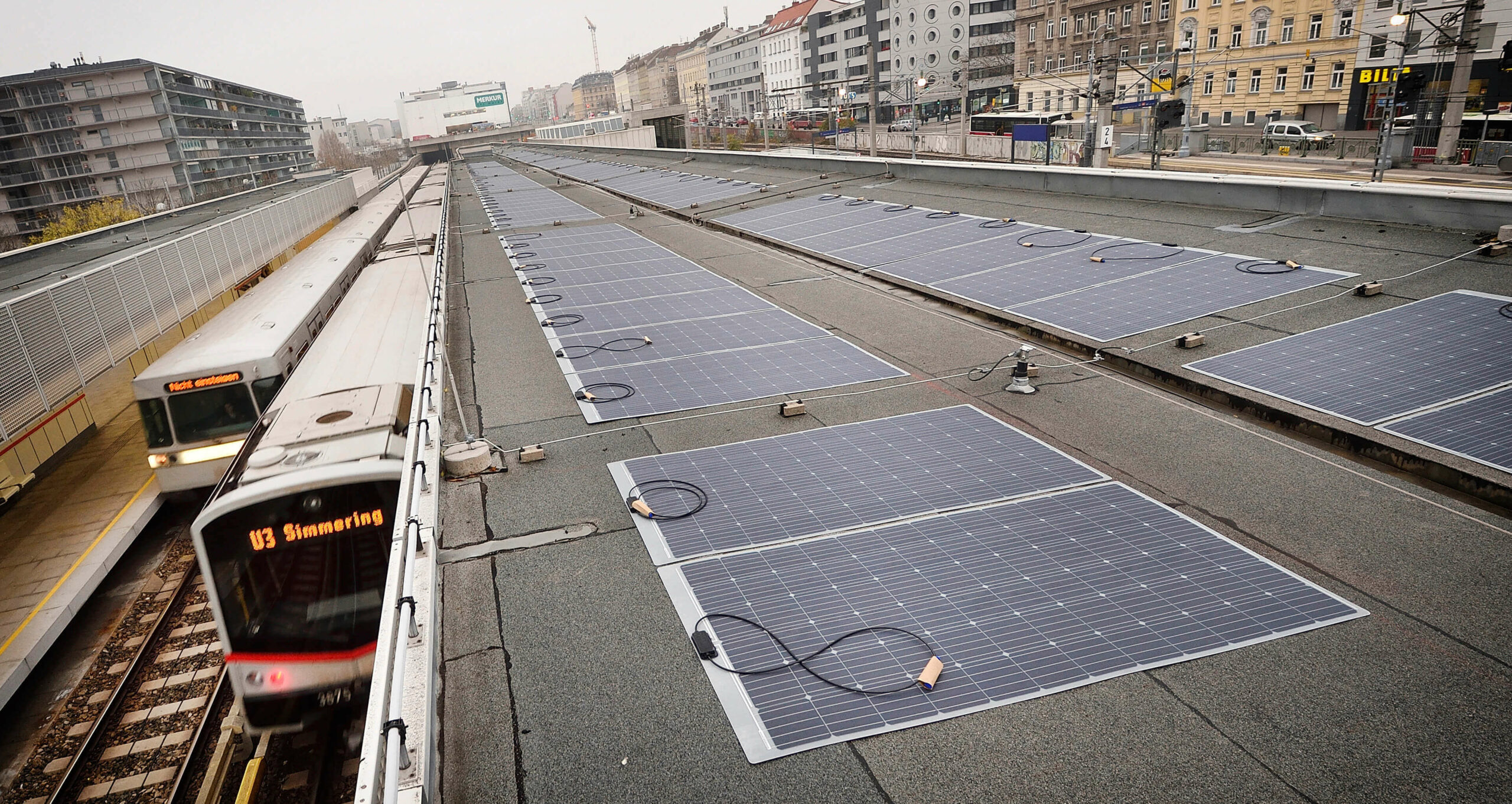 Solarmodule auf dem Dach der Wiener U-Bahn-Station Ottakring, umgeben von städtischen Gebäuden, bei dem eine U-Bahn einfährt.