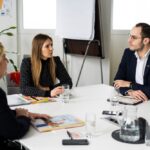 In einem Besprechungsraum diskutieren drei Personen an einem runden Tisch, umgeben von Papieren und Wassergläsern, im Hintergrund ein Flipchart. Diese Expert*innen der Zukunft gestalten schon heute die Ideen von morgen.