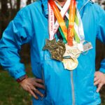 Person in einer blauen Jacke, die im Freien mehrere Marathon-Medaillen um den Hals trägt.