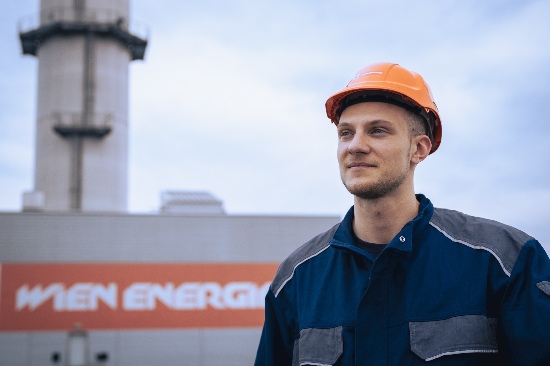Jakob Königshofer in Schutzhelm und Uniform, steht draußen neben einem Gebäude mit der Aufschrift „WIEN ENERGIE“.