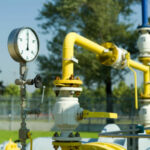 Nahaufnahme einer Gasleitung mit gelben Rohren und einem Druckmessgerät im Freien.