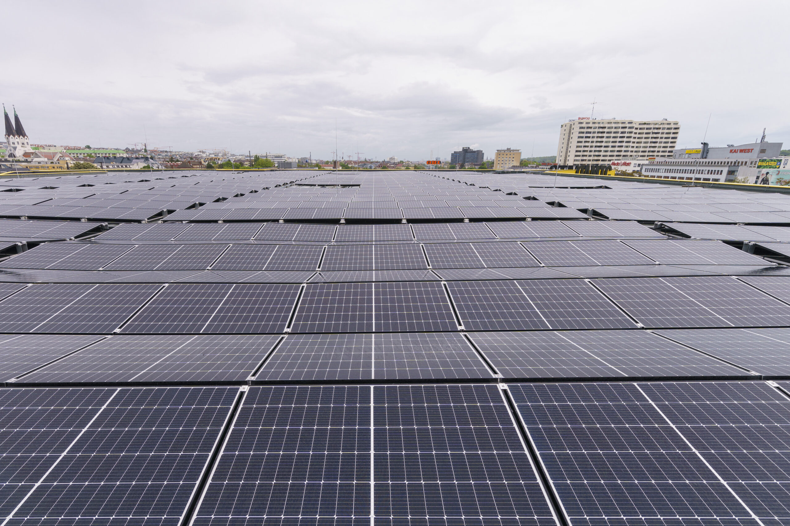 Eine riesige Anordnung von Solarmodulen auf dem Dach des ÖAMTC. In der Ferne ist unter einem bewölkten Himmel die Wiener Stadtlandschaft zu sehen.
