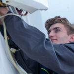 Techniker in grauer Uniform wartet eine Gastherme, wobei er sich auf Kabel und Komponenten konzentriert.