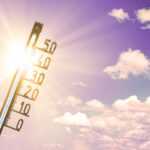 Ein Thermometer zeigt hohe Temperaturen vor einem sonnigen Himmel mit Wolken.
