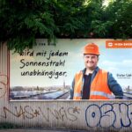 Plakatwand mit einem Mann mit Schutzhelm und Sicherheitsweste, der für Solarenergie wirbt, umgeben von Graffiti.