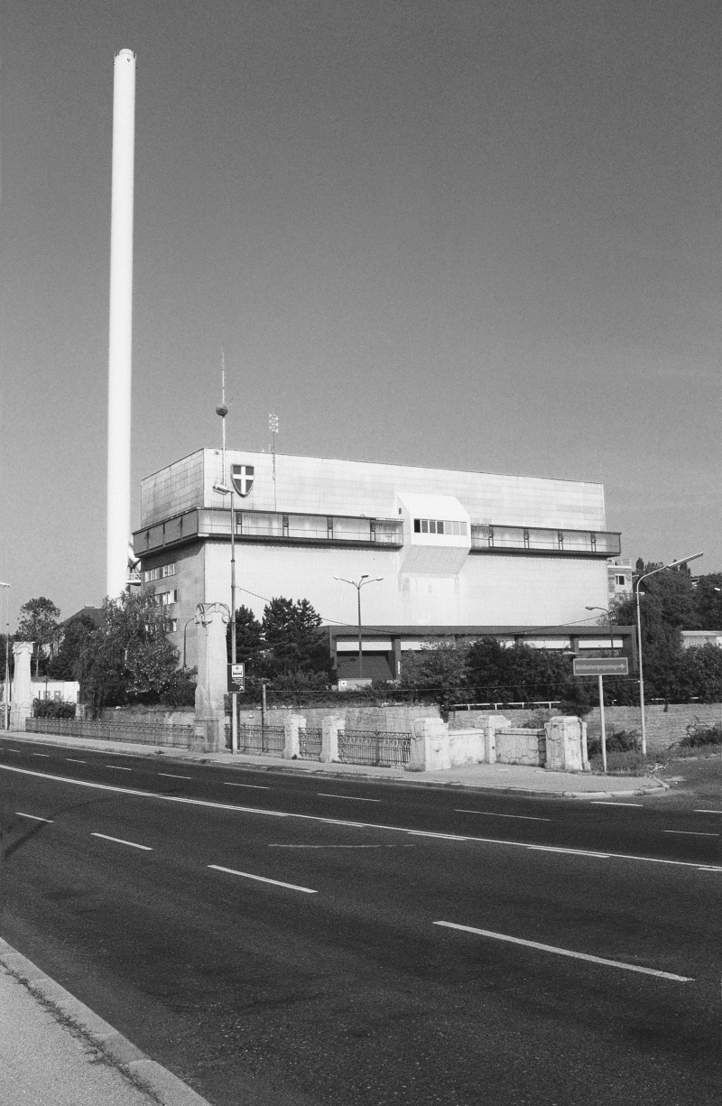 Das Schwarzweißbild zeigt das Flötzersteig Gebäude mit einem hohen Schornstein. Im Vordergrund befindet sich eine leere Straße.