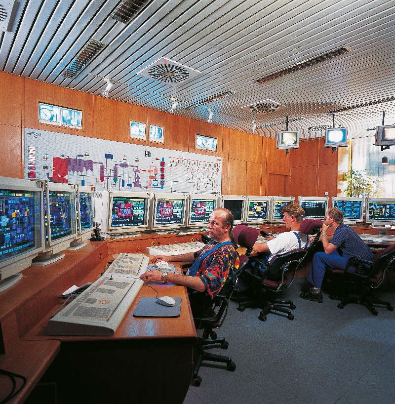 Personen, die in einem Kontrollraum - der Warte -  mit mehreren Computermonitoren arbeiten, auf denen verschiedene Daten und Diagramme angezeigt werden.