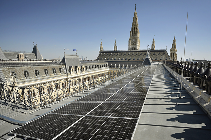 Sonnenkollektoren auf dem Dach des Rathauses mit dem Stephansdom im Hintergrund und blauem Himmel im Hintergrund.