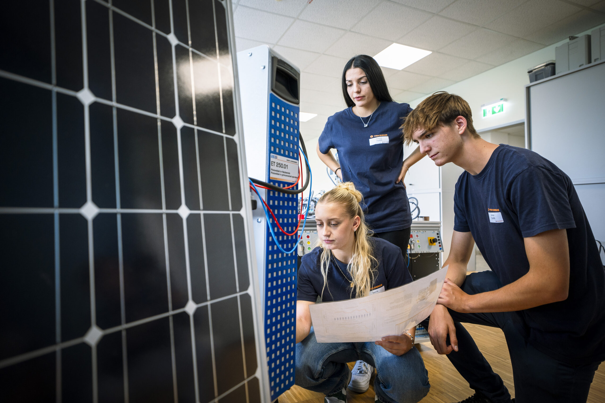 Drei Lehrlinge untersuchen im Ausbildungszentrum die Ausrüstung für Solarmodule und prüfen Dokumente.