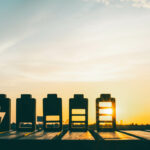 Silhouetten von Batteriesymbolen mit unterschiedlichen Ladezuständen vor einem Sonnenuntergangshimmel auf einer Holzoberfläche.