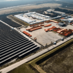 Luftaufnahme der weitläufigen Photovoltaikanlage Schafflerhofstraße mit ihren zahlreichen Paneelen neben einem Industriegebiet mit Containern und Gebäuden.
