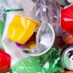 Ein Stapel wiederverwertbarer Gegenstände, darunter Dosen, Plastikflaschen, Papier und Aluminiumfolie in verschiedenen Farben.