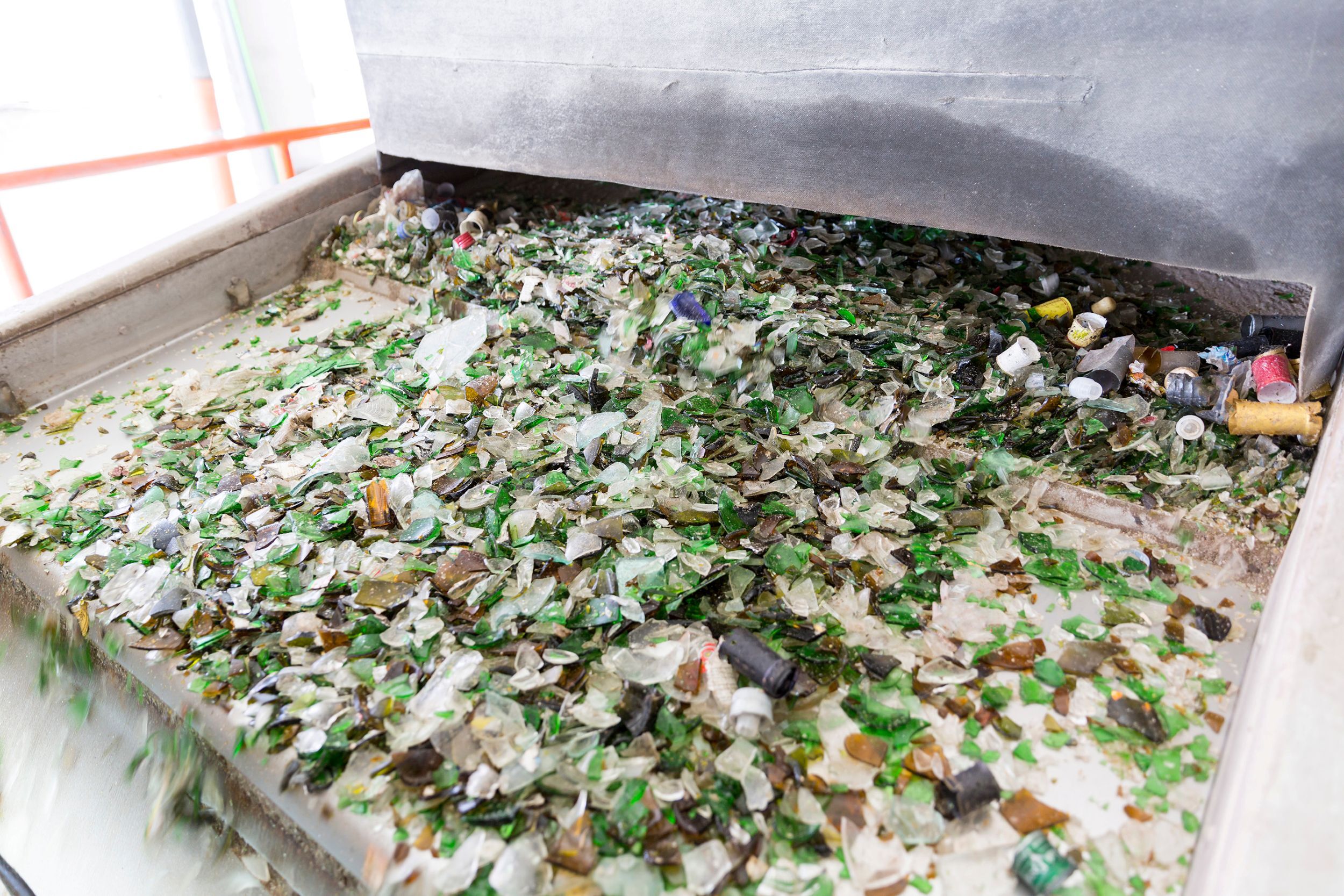 Zerbrochene Glasstücke und Kronkorken auf einem Förderband in einer Recyclinganlage.