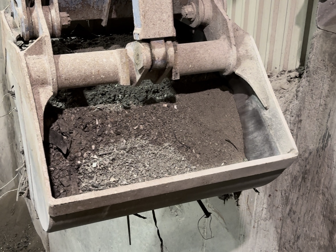 Eine Nahaufnahme einer Baggerschaufel, die eine Ladung Schlacke im Innenbereich trägt.