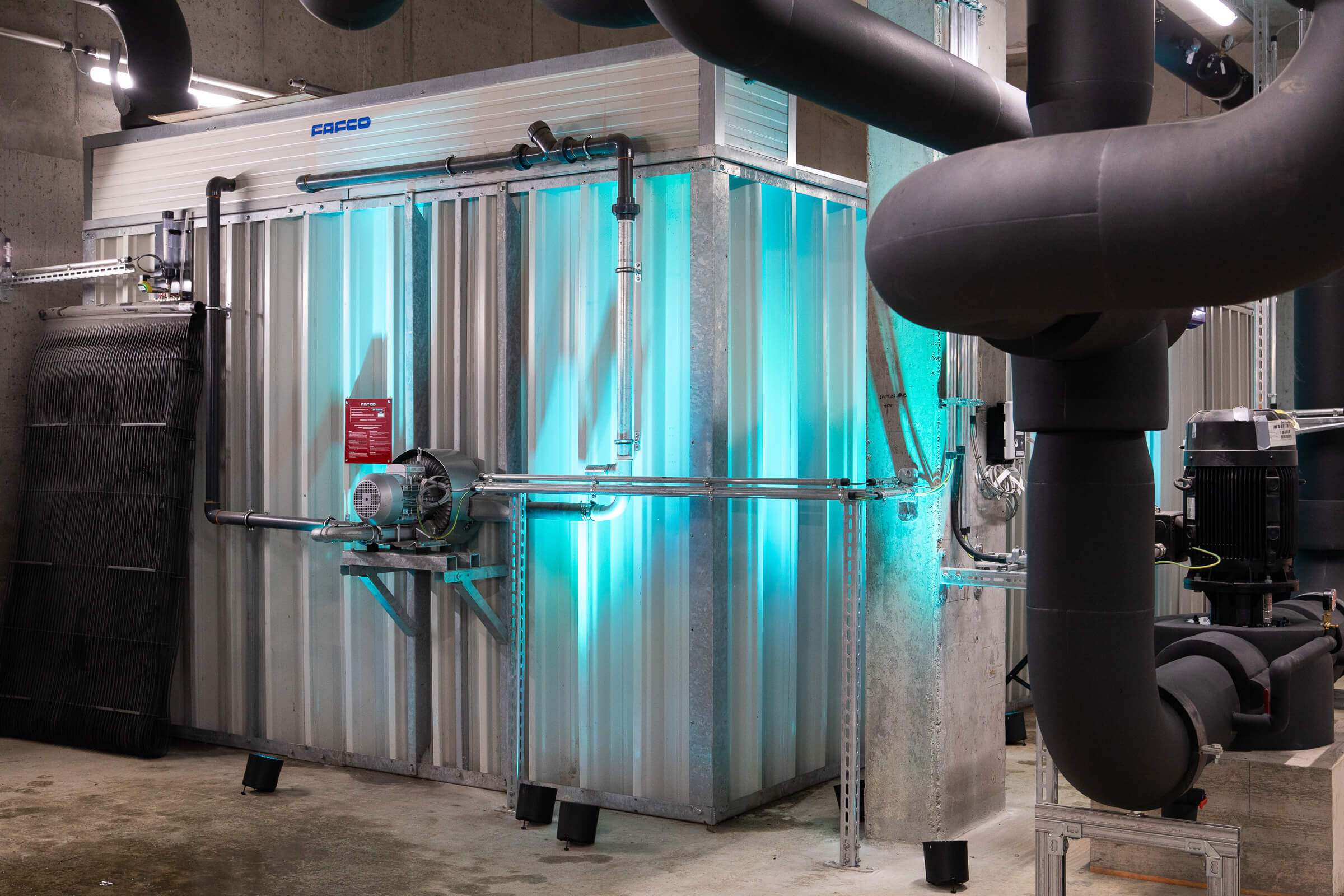 Große Industrieanlagen mit leuchtenden blauen Lichtern und schwarzen Rohren prägen das Bild der modernen Fernkältezentrale am MedUni Campus.