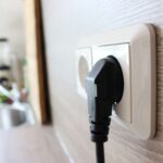 Ein schwarzer Stecker wird in eine weiße Wandsteckdose in einer Küche gesteckt.