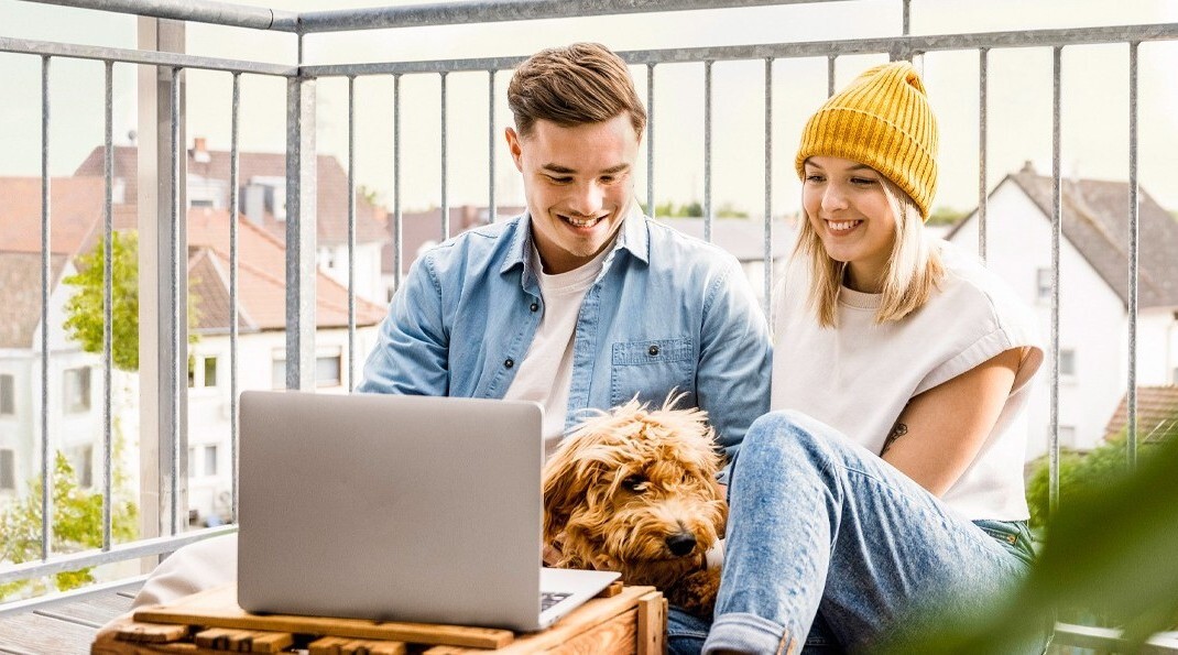 Ein Paar sitzt mit Laptop und Hund auf einem Balkon.