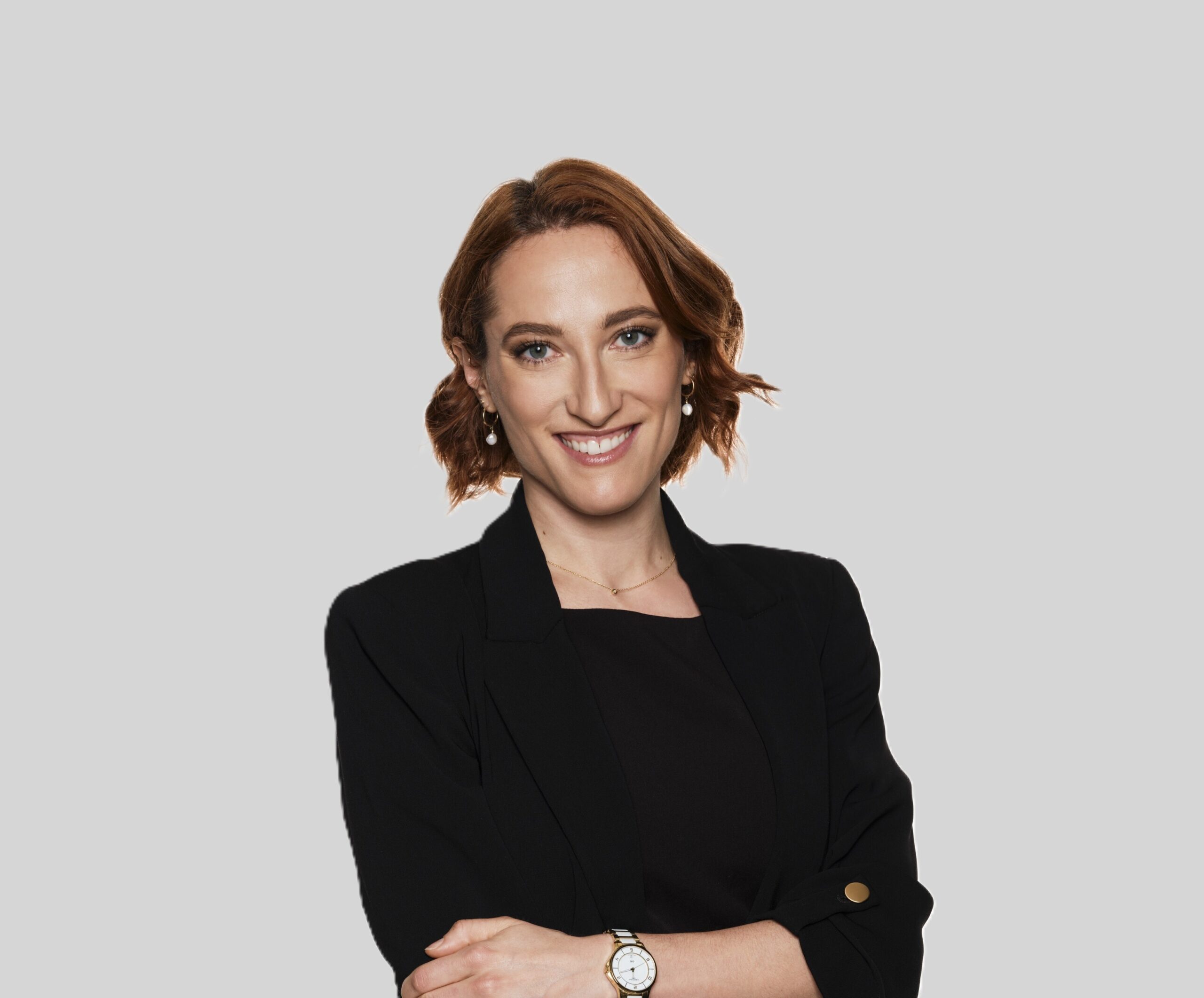 Lächelnde Frau mit kurzen kastanienbraunen Haaren in einem schwarzen Blazer vor einem schlichten grauen Hintergrund, identifiziert als Stefanie Marie Rupprecht.