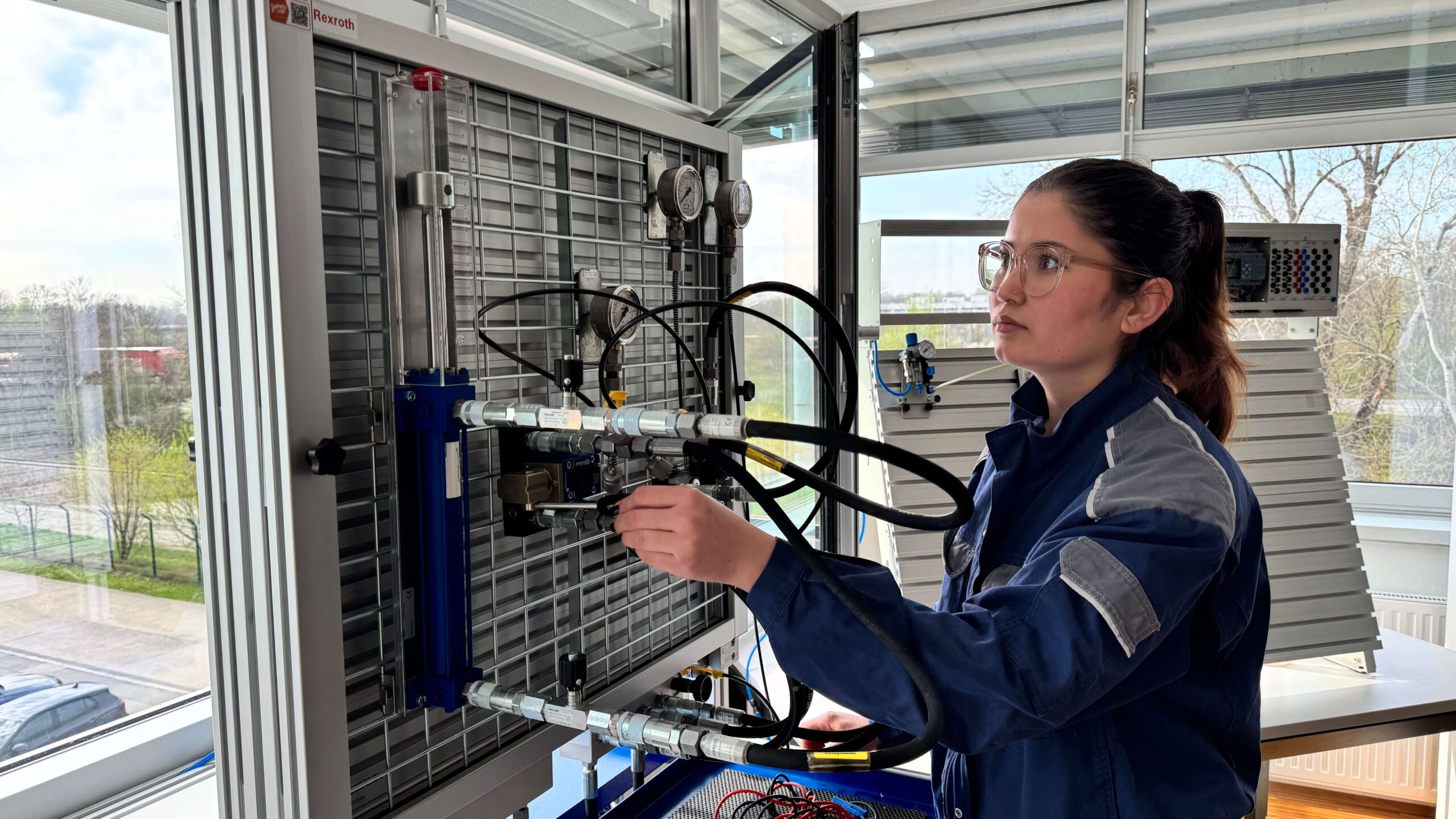 Eine Frau in blauer Uniform stellt in einem hellen, modernen Labor Kabel an einer technischen Schalttafel ein.