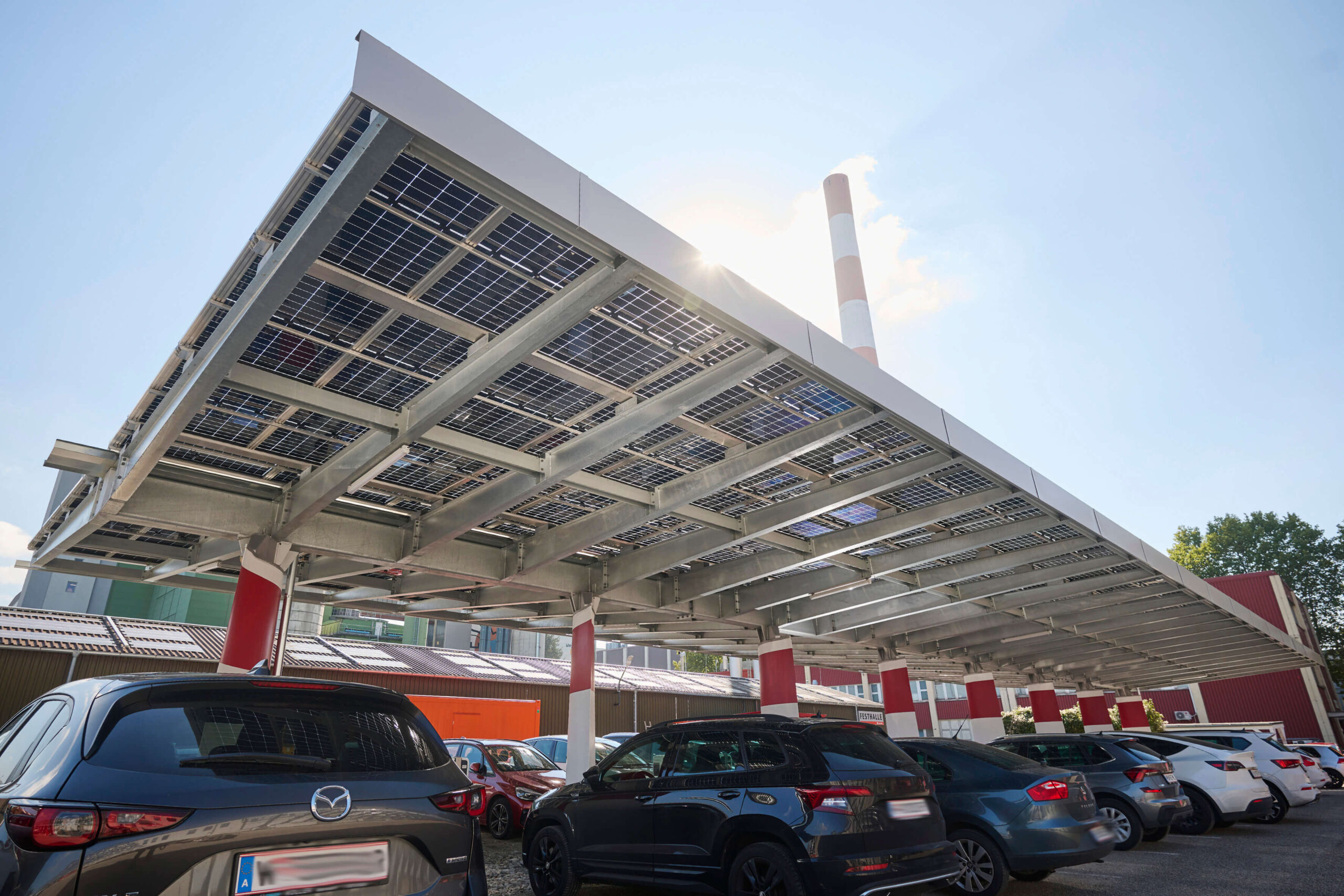 Ein Parkplatz mit Autos unter einem Vordach aus Sonnenkollektoren und Windrädern an einem sonnigen Tag.