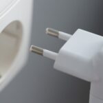 Eine Nahaufnahme einer Hand, die einen europäischen Steckeradapter in der Nähe einer Steckdose hält.
